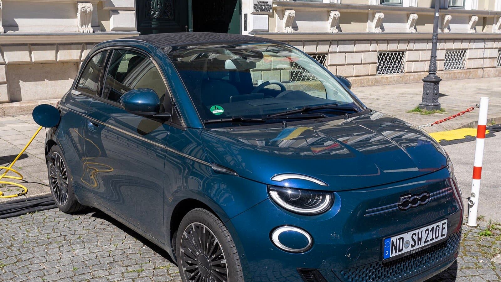 Fiat 500e használtan: sötétkék Fiat 500e elektromos autó töltés közben, rákötött töltőkábellel.
