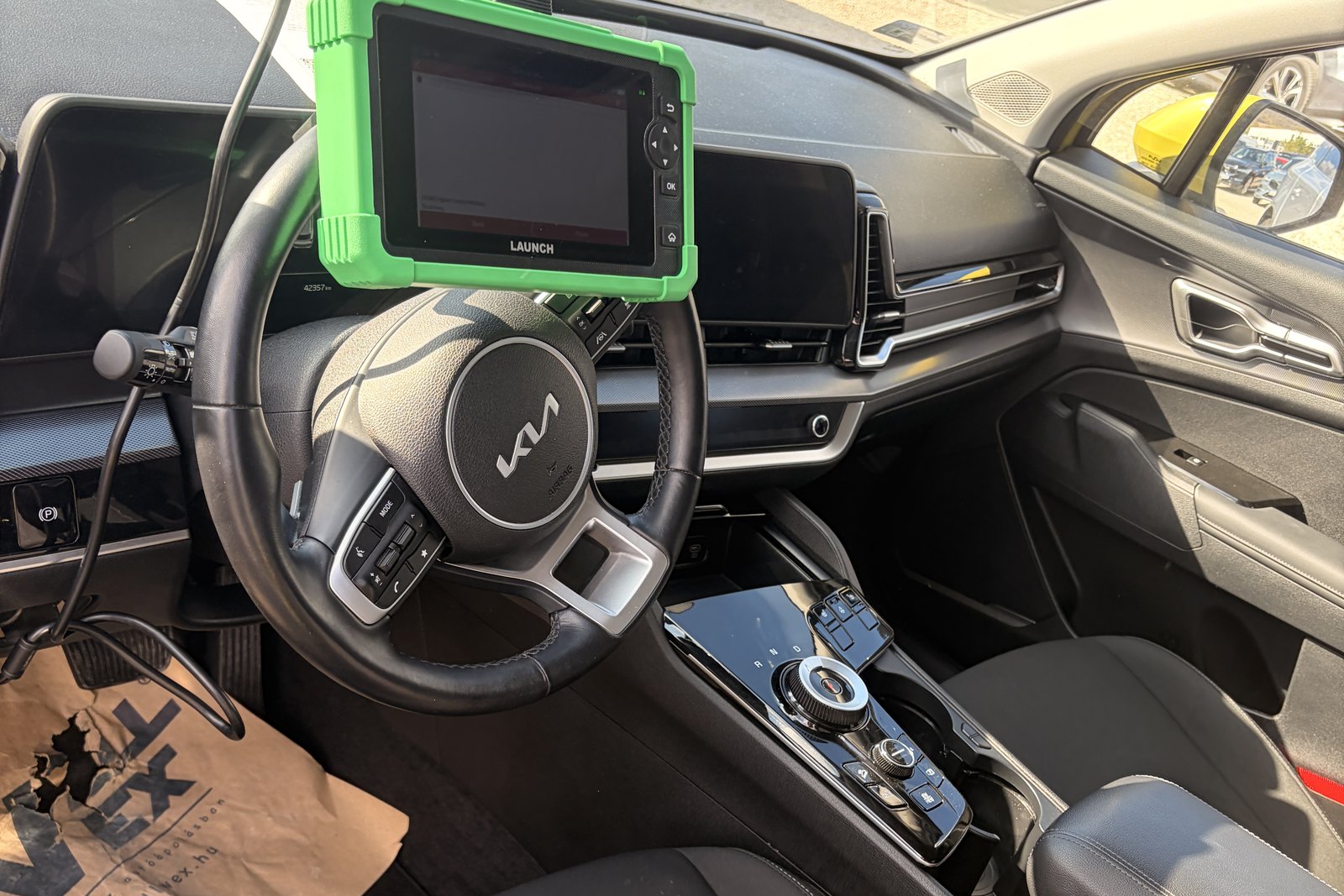 Launch diagnosztikai eszköz a Kia Sportage PHEV utasterében, a teljes rendszerlekérdezés közben, a műszerfal előtt. — EVX elektromos autó átvizsgálás és állapotfelmérés.
